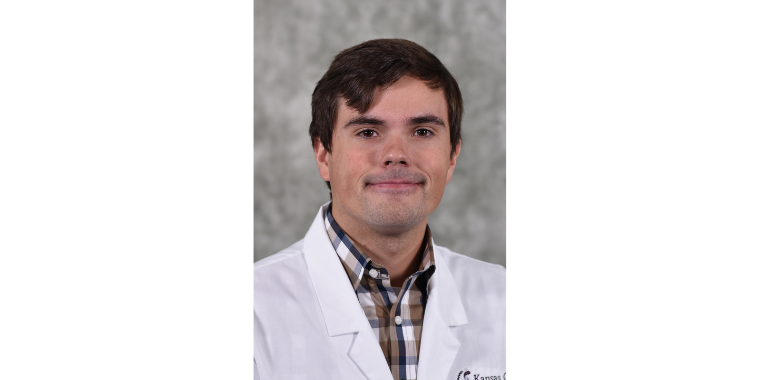 Tanner Movick smiles in his white coat in front of a gray background. 